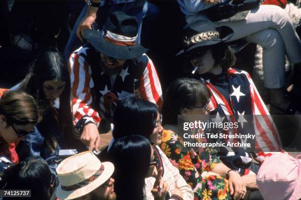 View of several attendees at the Monterey Pop Festival, Monterey, California, mid-June, 1967. Two men wear matching outfits that include flag-based...