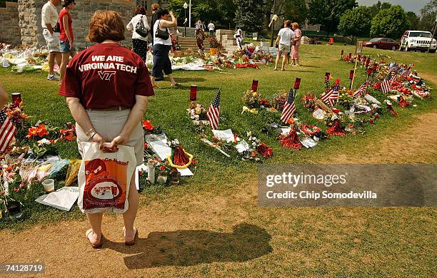 People walk along the edge of a large makeshift memorial, for all who died in last month's shooting rampage on campus, on the Drillfield in front of...