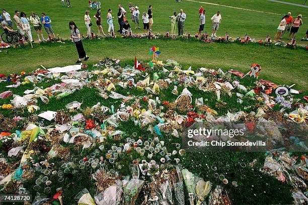 People walk along the edge of a large makeshift memorial, for all who died in last month's shooting rampage on campus, on the Drillfield in front of...