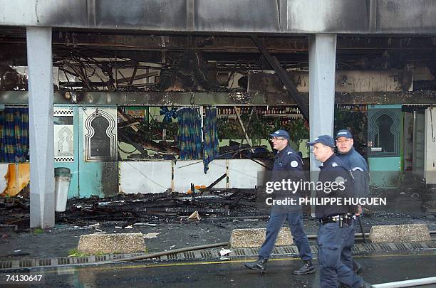 Mons-en-Bar?ul, FRANCE: Des policiers passent devant la facade d'un restaurant detruit par un incendie, le 12 mai 2007 dans une galerie marchande a...