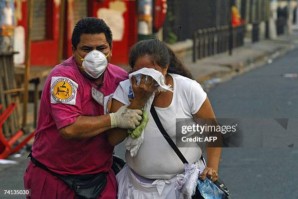 San Salvador, EL SALVADOR: Una mujer es auxiliada por un agente de cuerpos de socorro al ser afectada por gases lacrimogenos durante disturbios...