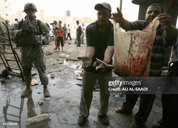 Soldier watches Iraqi show photographers bloody debris at the site of a powerful explosion which erupted 13 May 2007 in a central Baghdad market,...
