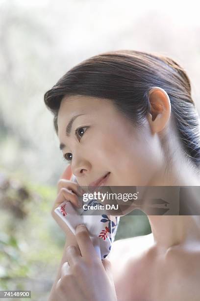 a mid adult woman putting tenugui on her cheek and tilting her head to the right, side view, close up - 手ぬぐい ストックフォトと画像