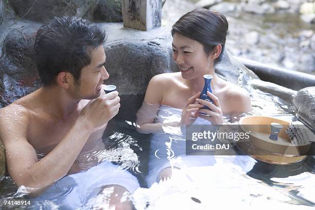 mid adult couple sitting in the outdoor hot spring bath, drinking sake, front view, side view - 手ぬぐい ストックフォトと画像