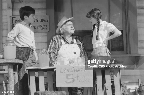 American actor Will Geer opines from behind a lemonade stand as fellow cast members and American child actors David Harper and Kami Cotler listen...