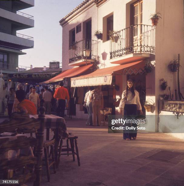 View of pedestrian traffic at several outdoor cafes, probably La Nogalera in Torremolinos, Southern Spain, June 1970.