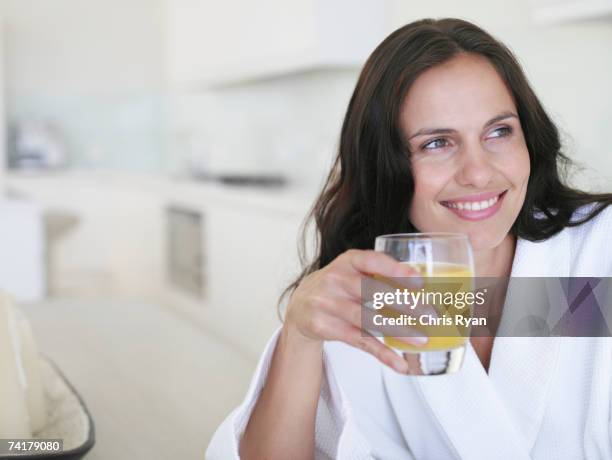 mujer en la bata de baño, con vaso de jugo de naranja sonriendo - zumo de naranja fotografías e imágenes de stock