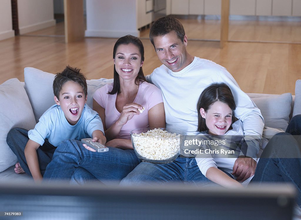Man and woman with boy and girl watching television and eating popcorn