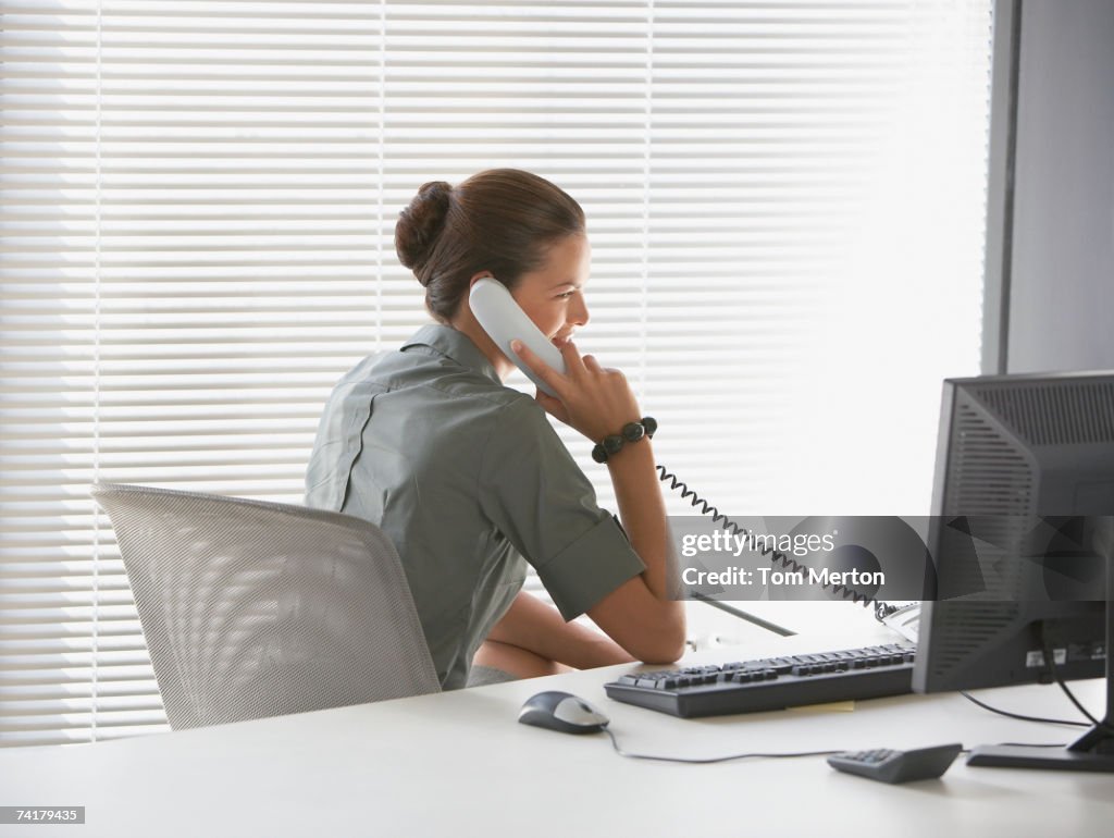 Rear view of businesswoman sitting at desk talking on telephone