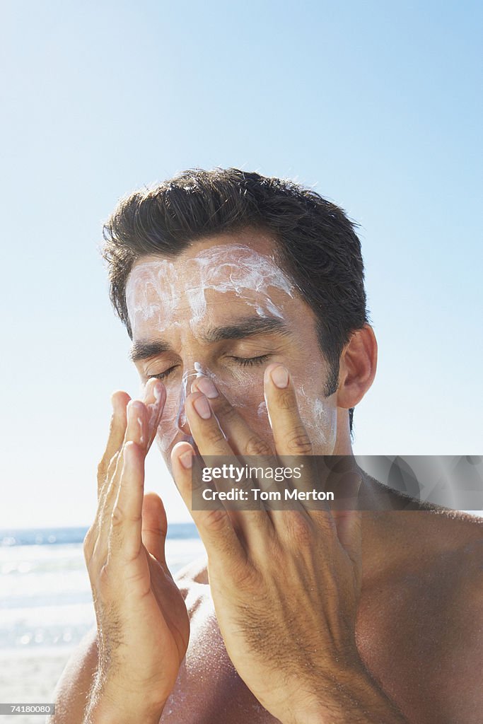 Man applying sun block or suntan lotion to face