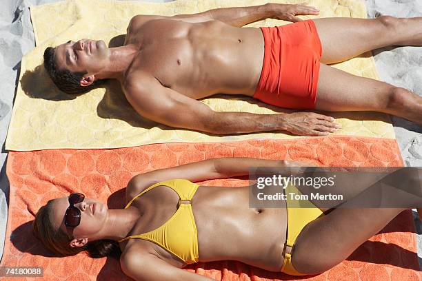 man and woman sunbathing on beach towels in sand - zwembroek stockfoto's en -beelden