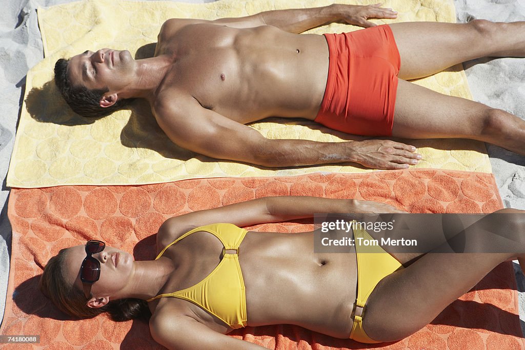 Man and woman sunbathing on beach towels in sand