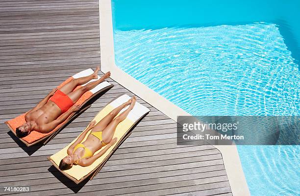 hombre y una mujer tomando el sol en la terraza de la piscina - tomar sol fotografías e imágenes de stock