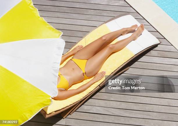 frau sonnenbaden am pool deck im bikini mit regenschirm - sonnenbaden stock-fotos und bilder