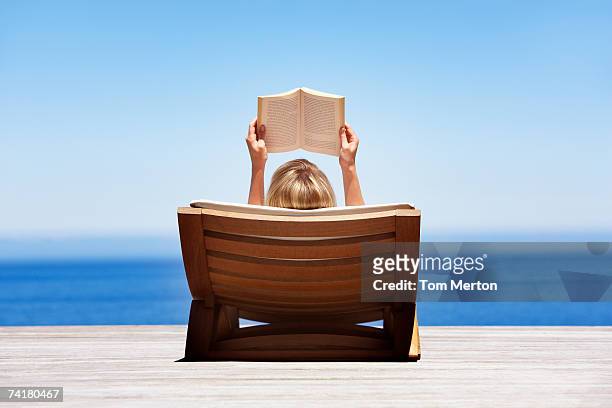 vista posterior de lectura de mujer en silla de madera al aire libre - libro verano fotografías e imágenes de stock