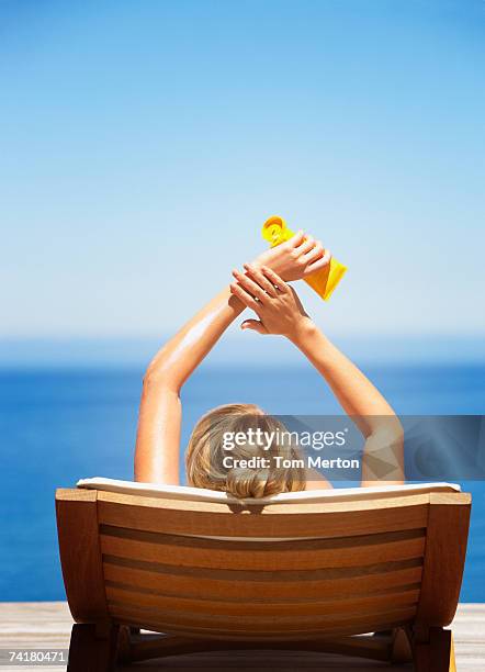 rear view of woman on folding chair outdoors applying sun block or suntan lotion - applying sunscreen stock pictures, royalty-free photos & images