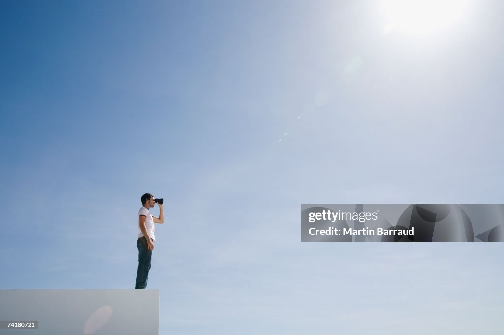 Mann auf Sockel mit Fernglas und blauer Himmel im Freien
