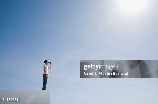Hombre en pedestal con binoculares y azul cielo al aire libre Hombre en pedestal con binoculares y azul cielo al aire libre