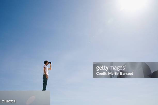 uomo su piedistallo con binocolo e blu cielo aperto - scoperta foto e immagini stock