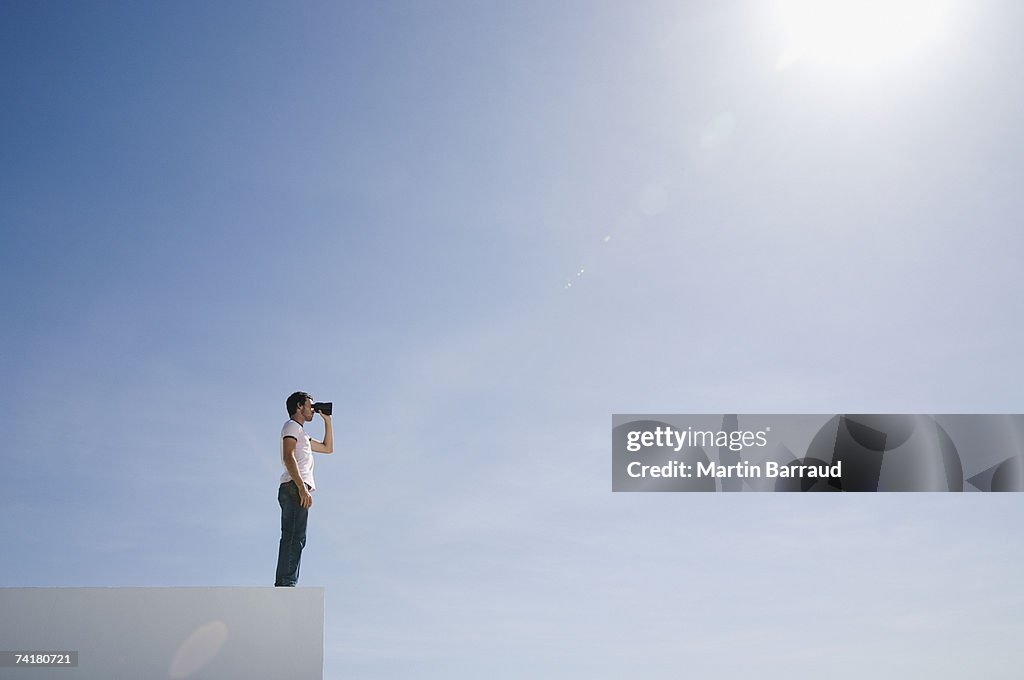 Man on pedestal with binoculars and blue sky outdoors