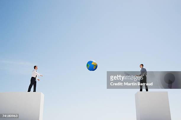 two businessmen tossing standing on walls with large gap tossing globe - big world stock pictures, royalty-free photos & images