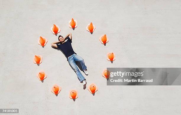 man lying down in circle of traffic cones with arms up - road cone stock pictures, royalty-free photos & images