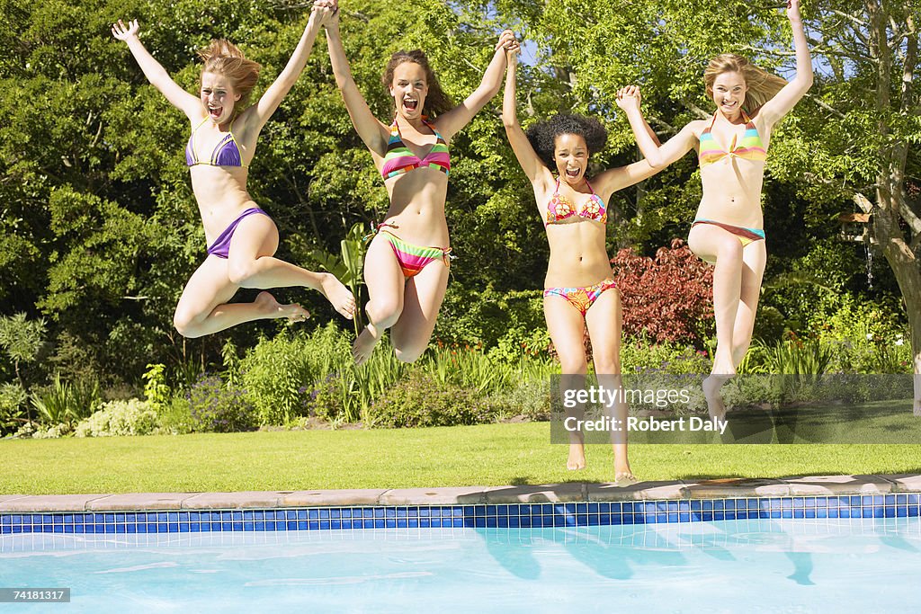 Four teenage girls jumping into pool