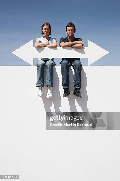 man and woman sitting on wall outdoors with blank arrow - opposite direction stockfoto's en -beelden