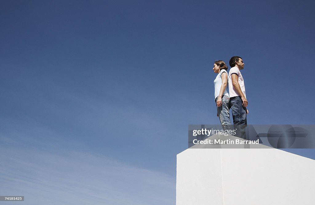 Man and woman standing on box back to back outdoors with blue sky