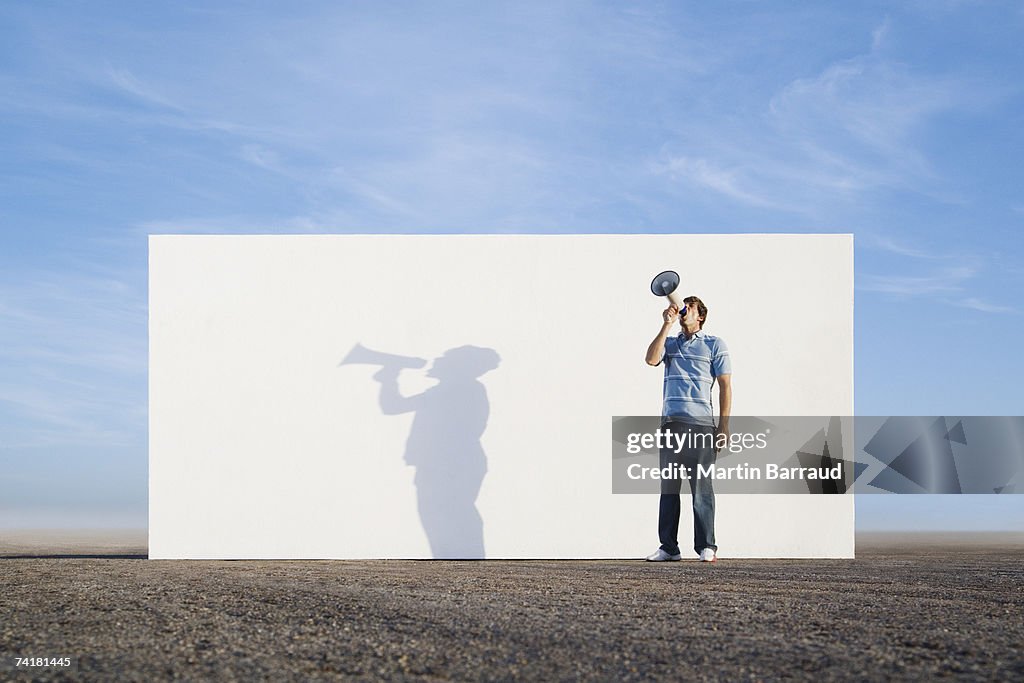 Man standing in front of wall outdoors with megaphone and shadow