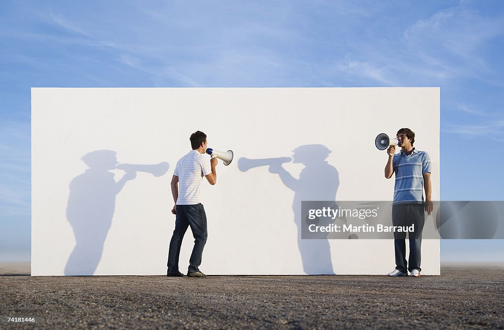 Men standing in front of wall outdoors with megaphones and shadows