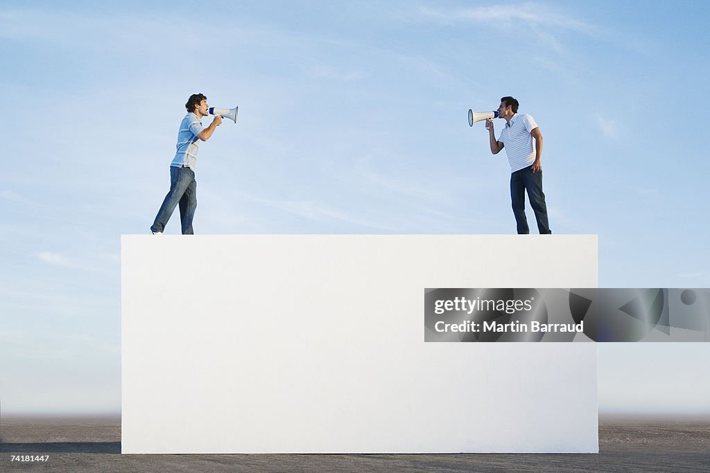 Men standing on wall outdoors with megaphones