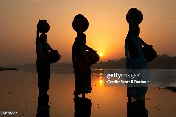 "agra, uttar pradesh, india. women are silhouetted against the rising sun as they balance water jugs on their heads while collecting fresh water at the yamuna river near the taj mahal." - wt1 foto e immagini stock