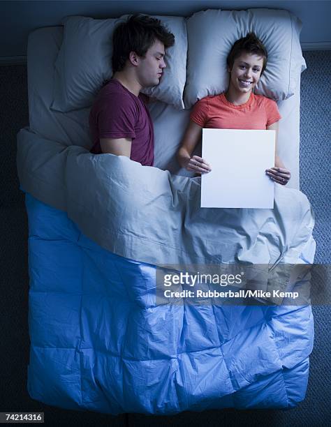 man asleep in bed and woman holding blank sign smiling - mike storen stockfoto's en -beelden