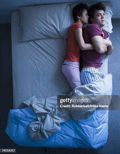 sleeping woman snuggling awake man in bed - mike storen stockfoto's en -beelden