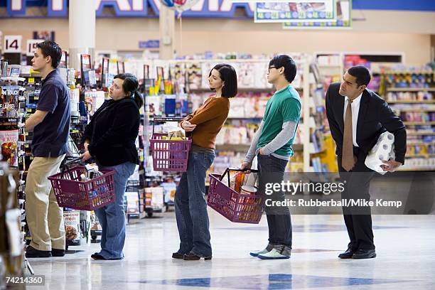 people waiting in line with shopping baskets at grocery store - schlange stock-fotos und bilder