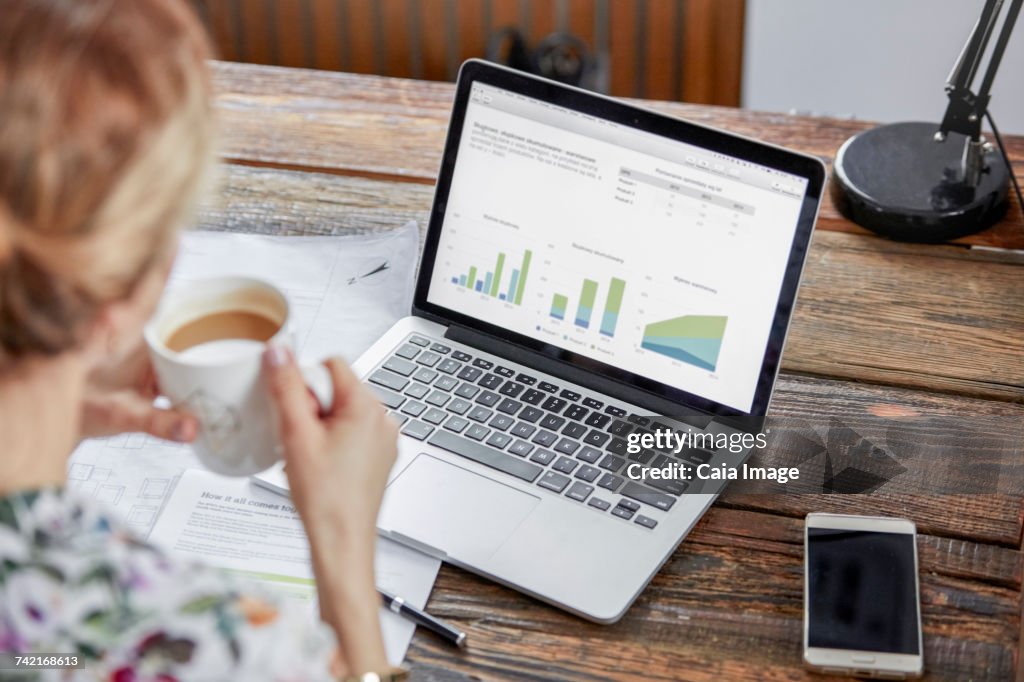 Businesswoman drinking tea and reviewing data at laptop