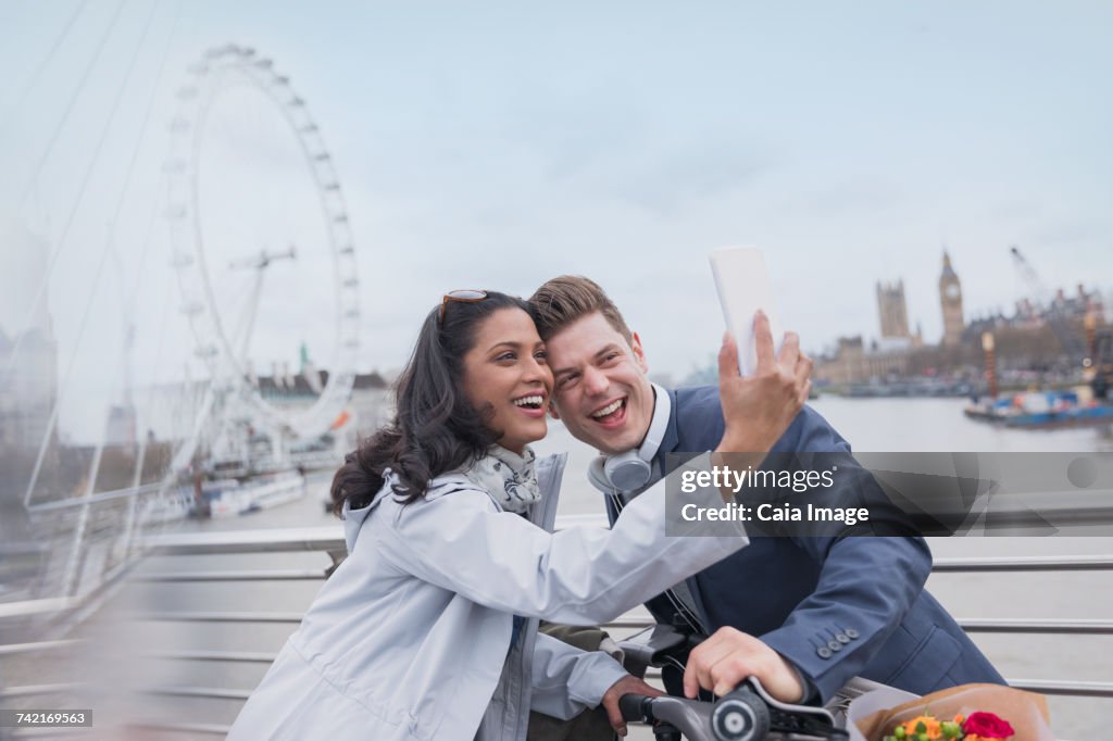 Smiling couple tourists taking selfie with camera phone on bridge near Millennium Wheel, London, UK