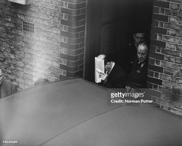 John Christie hides his face as he leaves West London Police Court after a remand hearing, 15th April 1953. Christie is accused of his wife's murder...
