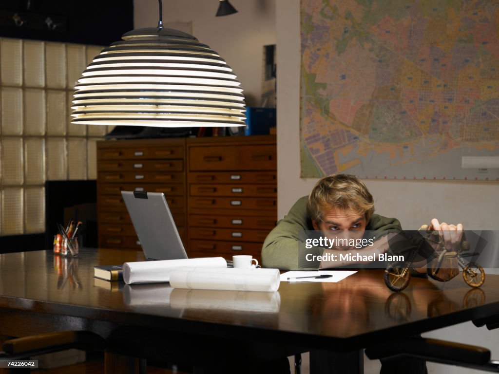 Man playing with model motorcycle at desk in office