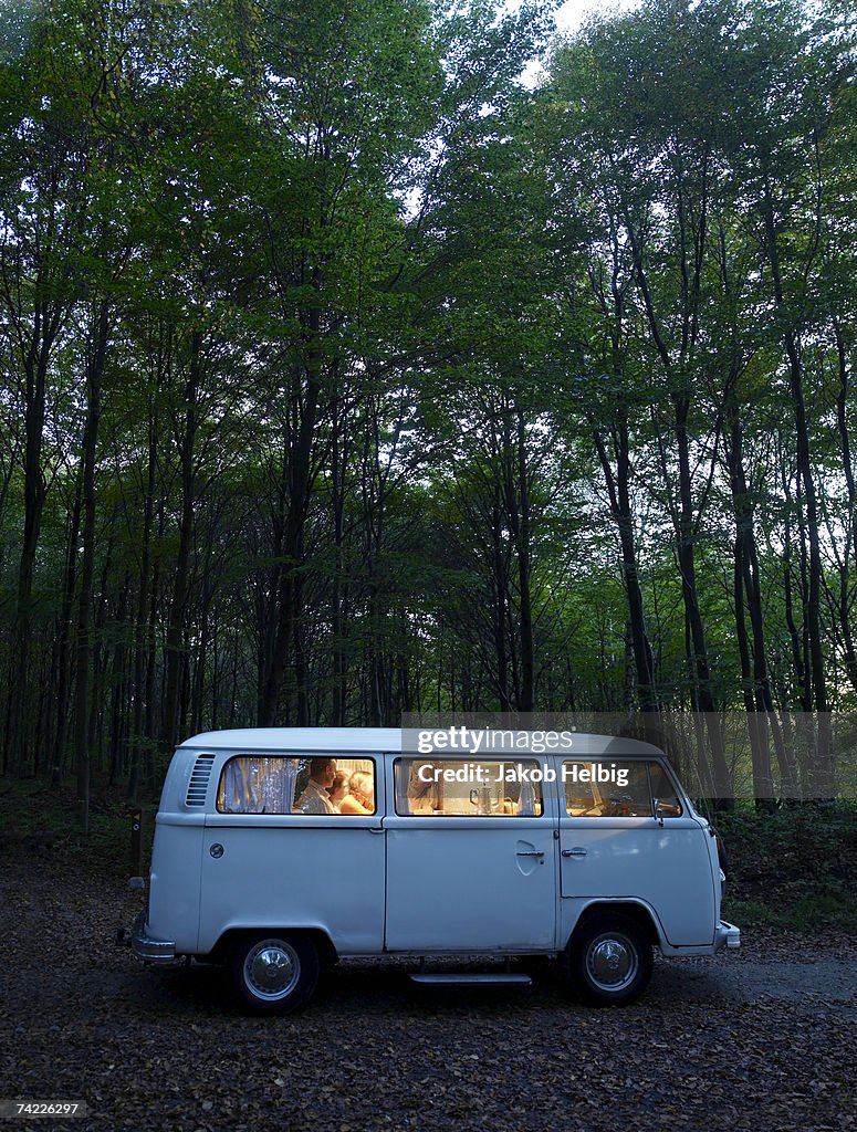 "Family in illuminated van in forest, side view, evening"