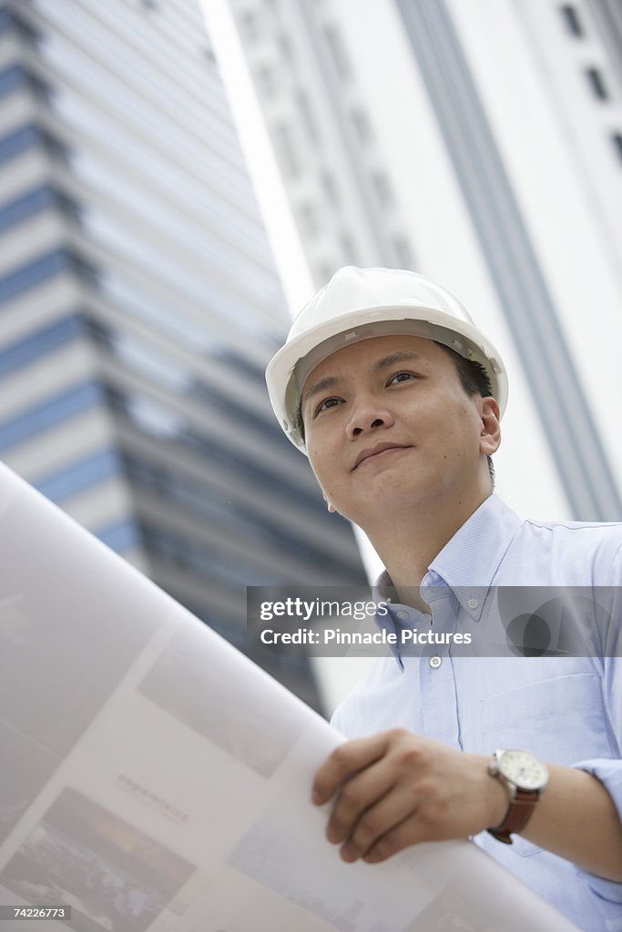 Architect wearing hardhat holding blueprint outdoors, low angle view