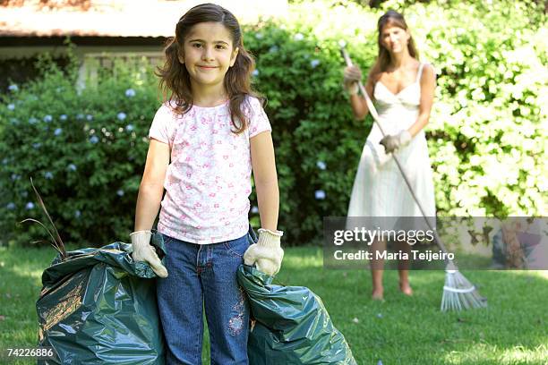 "mother and daughter (7-8) in garden, daughter holding garbage bag, mother raking grass" - trash bag dress stock pictures, royalty-free photos & images