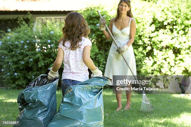 mother and daughter (6-7) in garden, daughter holding garbage bag, mother raking grass - trash bag dress stock pictures, royalty-free photos & images