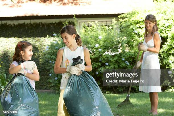 two sisters (7-11) and mother gardening, smiling - trash bag dress stock pictures, royalty-free photos & images