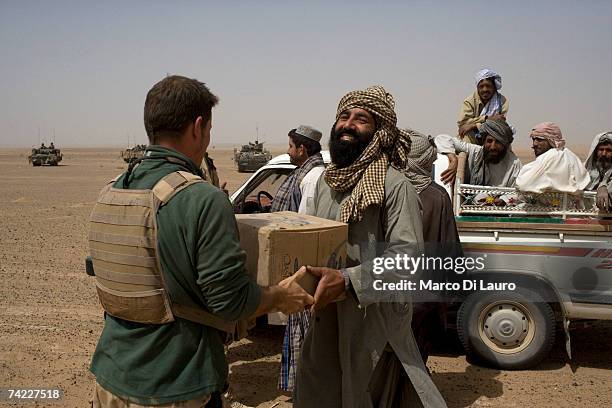 British soldier from the B Squadron of the Light Dragoons Regiment hands bottles of water to local Afghans at a vehicle checkpoint while conducting...