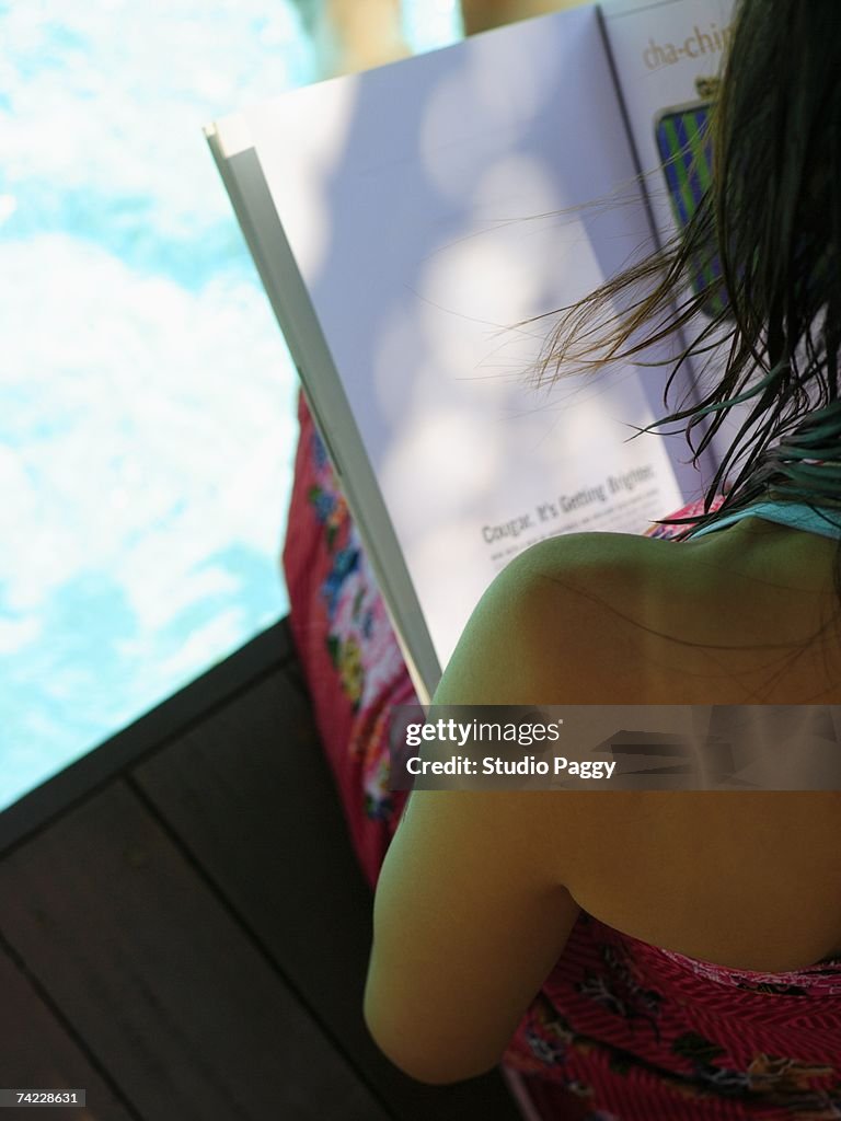 Rear view of a woman reading a book at the poolside