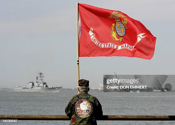 New York, UNITED STATES: A man holding a US Marine Corp flag watches as ships sail past the Statue of Liberty in New York Harbor 23 May, 2007. The...