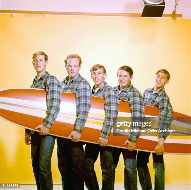 Rock and roll band "The Beach Boys" pose for a portrait with a surfboard in August 1962 in Los Angeles, California. Brian Wilson, Mike Love, Dennis...