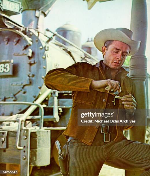 Country singer/songwriter Johnny Cash wears a gun in a holster and a cowboy hat as he gets his hands dirty in front of a train in circa 1965.